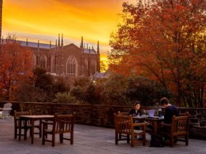 The sun sets over Duke Chapel, as viewed from the tables in front of the Perkins library 